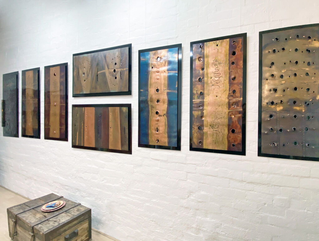 Exhibition showcasing 8 finished pieces of copper art. All hanging side by side in portrait and with two hanging on top of each other in landscape, on the white studio wall.